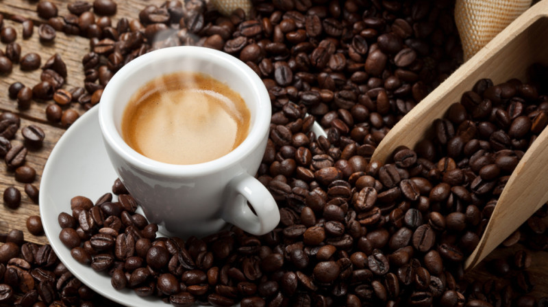 immagine di una tazza di caffè fumante con i chicchi di caffè vicino